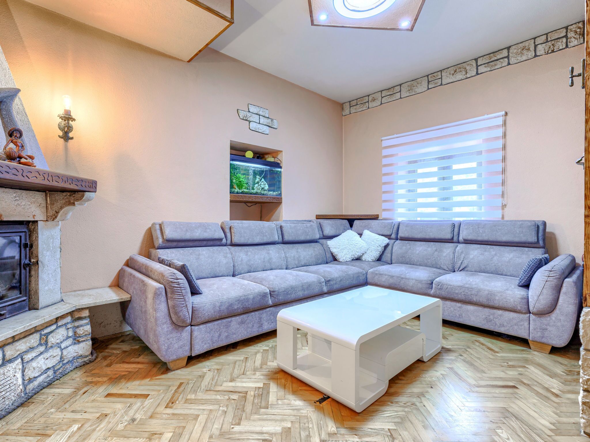 Een woonkamer met een visgraat houten vloer, een grijze modulaire bank, een witte salontafel, een open haard en een accentmuur van steen.