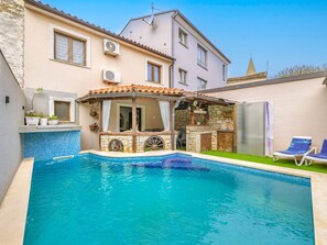 Ein Swimmingpool mit einer Sonnenterrasse aus Stein und Holz, einer Bar und Liegestühlen.
