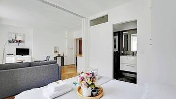 A modern hotel room with a bed, grey sofa, and a small kitchenette.