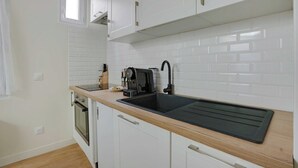 A modern kitchen with white cabinets, a black sink, and a built-in oven. - Cosy Apt - 2P - République / Marais (Paris)