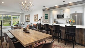 Een moderne keuken met witte kastjes, een roestvrijstalen koelkast en een houten eettafel met stoelen.