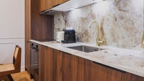 Una cocina con armarios de madera, encimera de mármol, un lavamanos y una cafetera.