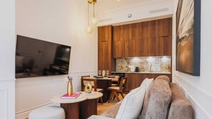Una sala moderna con un sofá, reposapiés y un comedor con mesa y sillas. Se ve una cocina con armarios de madera y encimera al fondo.
