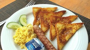 Un plato de desayuno con tostadas, huevos revueltos, una salchicha y un recipiente de yogur.