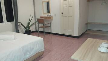 A hotel room with a bed, a desk, a chair, a potted plant, a wardrobe, and a small table with a cup and saucer.