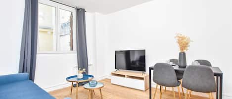 Ein modernes Wohnzimmer mit einer Couch, einem Fernseher, einem Esstisch mit Stühlen und einem kleinen Beistelltisch.