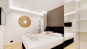 Ein modernes Schlafzimmer mit einem großen Bett, einem an der Wand montierten Fernseher und einem runden Wandkunstwerk.