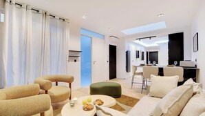 Ein modernes Wohnzimmer mit einer Couch, Sesseln, einem Esstisch mit Frühstück und einer Küche im Hintergrund.