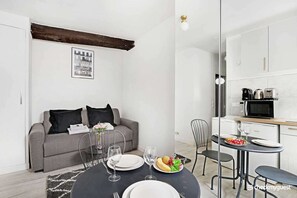 Un espacio moderno para vivir con comedor, kitchenette y un sofá gris con cojines negros.
