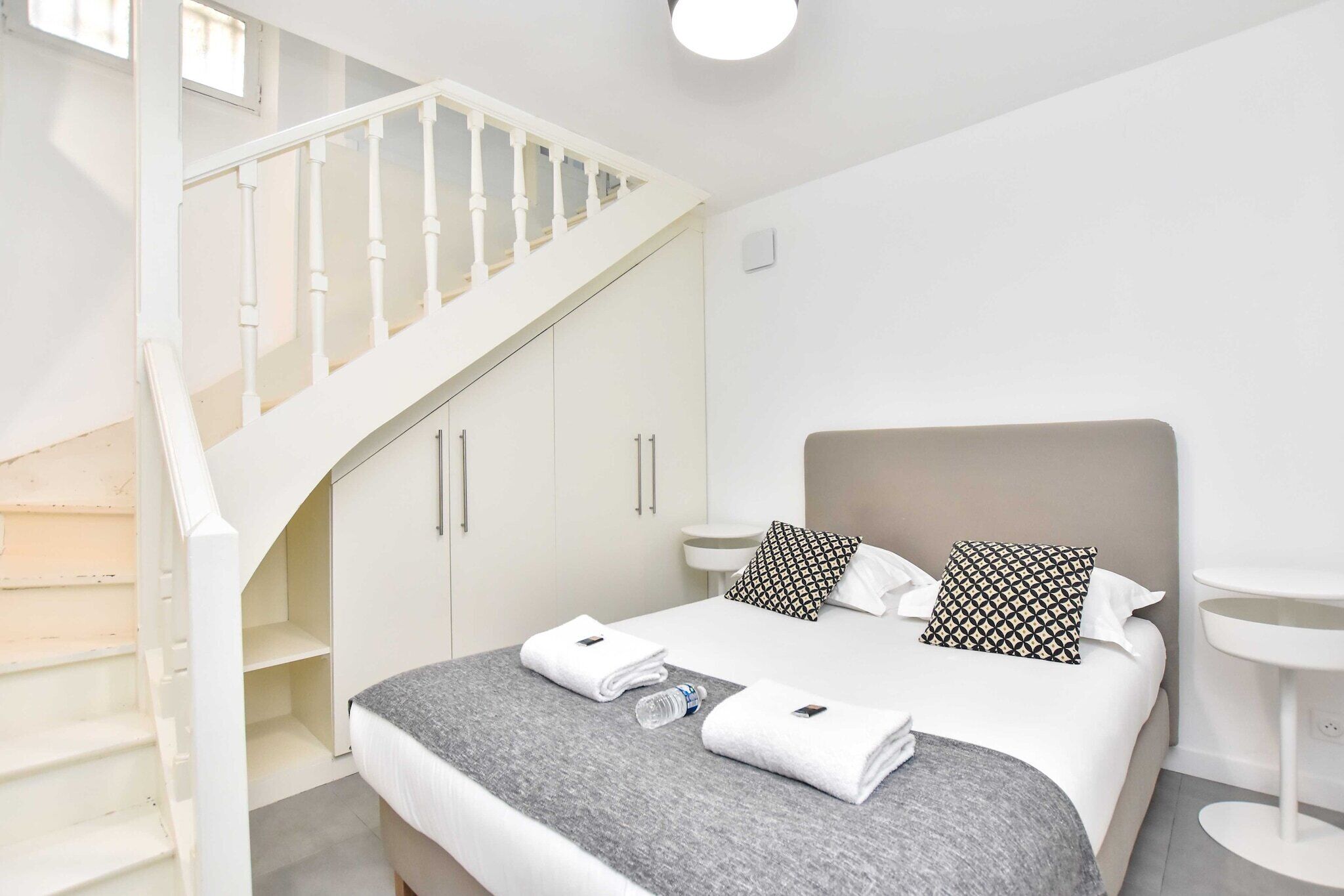 A bedroom with a bed, white wardrobe, and a staircase.
