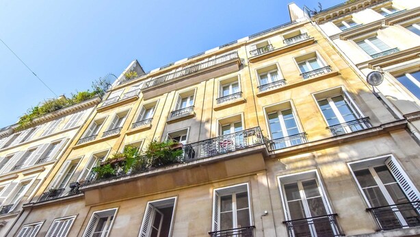 Un immeuble à plusieurs étages, doté de balcons, de grandes fenêtres et surplombant un ciel dégagé.