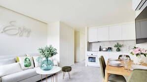 A modern kitchen with white cabinets, a dining area with a wooden table and chairs, and a living room with a sofa and decorative pillows. - Charming apartment - 1BR/4P - Faubourg-du-Roule (Paris)