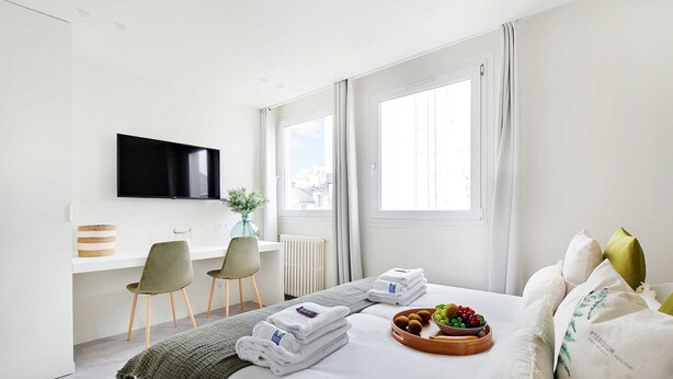 A hotel room with a bed, a desk with two chairs, a TV, and a window with curtains. - Charming apartment - 1BR/4P - Faubourg-du-Roule (Paris)
