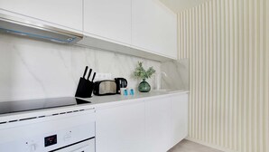 A modern kitchen with white cabinets, a stove, a toaster, a kettle, and a vase with green plants. - Charming apartment - 1BR/4P - Faubourg-du-Roule (Paris)