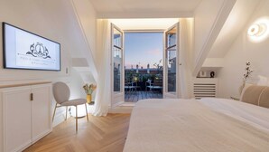 Een slaapkamer met een groot bed, een stoel, een bureau en een stadszicht door open deuren.