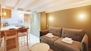 Ein modernes Wohnzimmer mit einer Couch, einem Essbereich mit Tisch und Stühlen sowie einer Küche im Hintergrund.