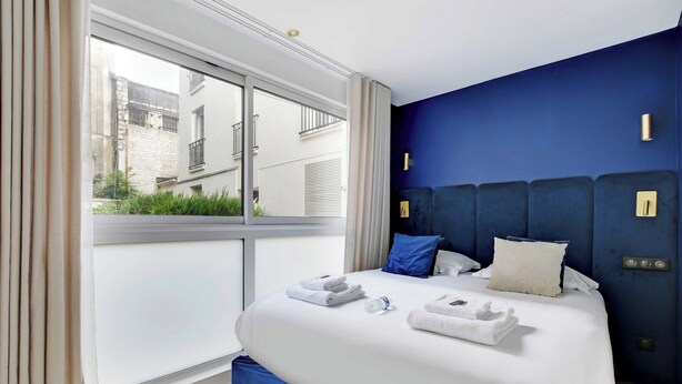 Habitació d'hotel moderna amb un llit gran, vista a la ciutat i una paret d'accent blava.
