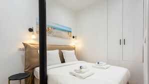 A neatly made bed with white linens and towels, a small bedside table, a wall-mounted light, and a painting of a beach scene. - Intimate apartment - 1BR/4P - Oberkampf (Paris)