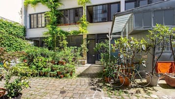 Une cour avec des plantes en pot, un vélo et un bâtiment doté d’un escalier.