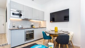 A modern kitchen with built-in appliances, a dining area with a round table and chairs, and a flat-screen TV mounted on the wall. - Intimate apartment - 1BR/4P - Oberkampf (Paris)