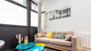 A modern living room with a sofa, a small table, and a window. - Intimate apartment - 1BR/4P - Oberkampf (Paris)