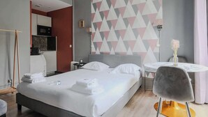 Una habitación de hotel moderna con una cama, una mesa redonda de comedor con una silla, una pequeña cocina y un adorno en la pared.