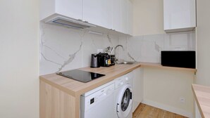 Cocina compacta con armarios blancos, lavadora, cafetera y una tableta sobre la encimera.