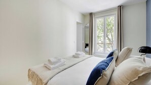 Un dormitorio con cama, mesita de noche, lámpara y ventana con cortinas.