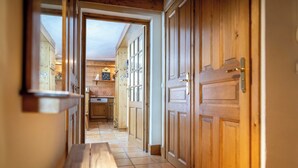 Un corridoio in legno con una panca, porte in legno e una zona cucina visibile attraverso un'apertura.