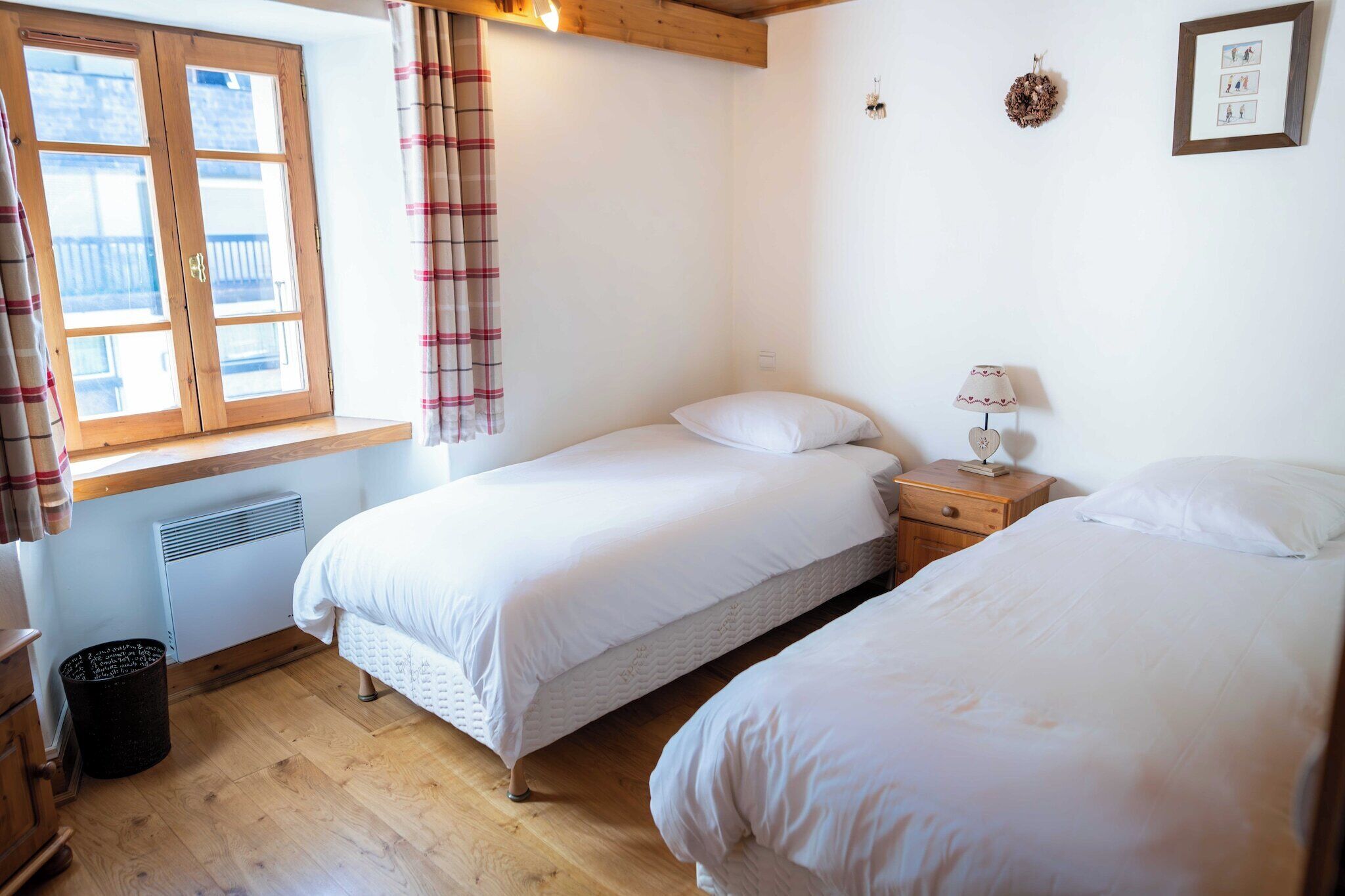 Un dormitorio con dos camas individuales, una ventana con cortinas, una mesita de noche con lámpara y un radiador.
