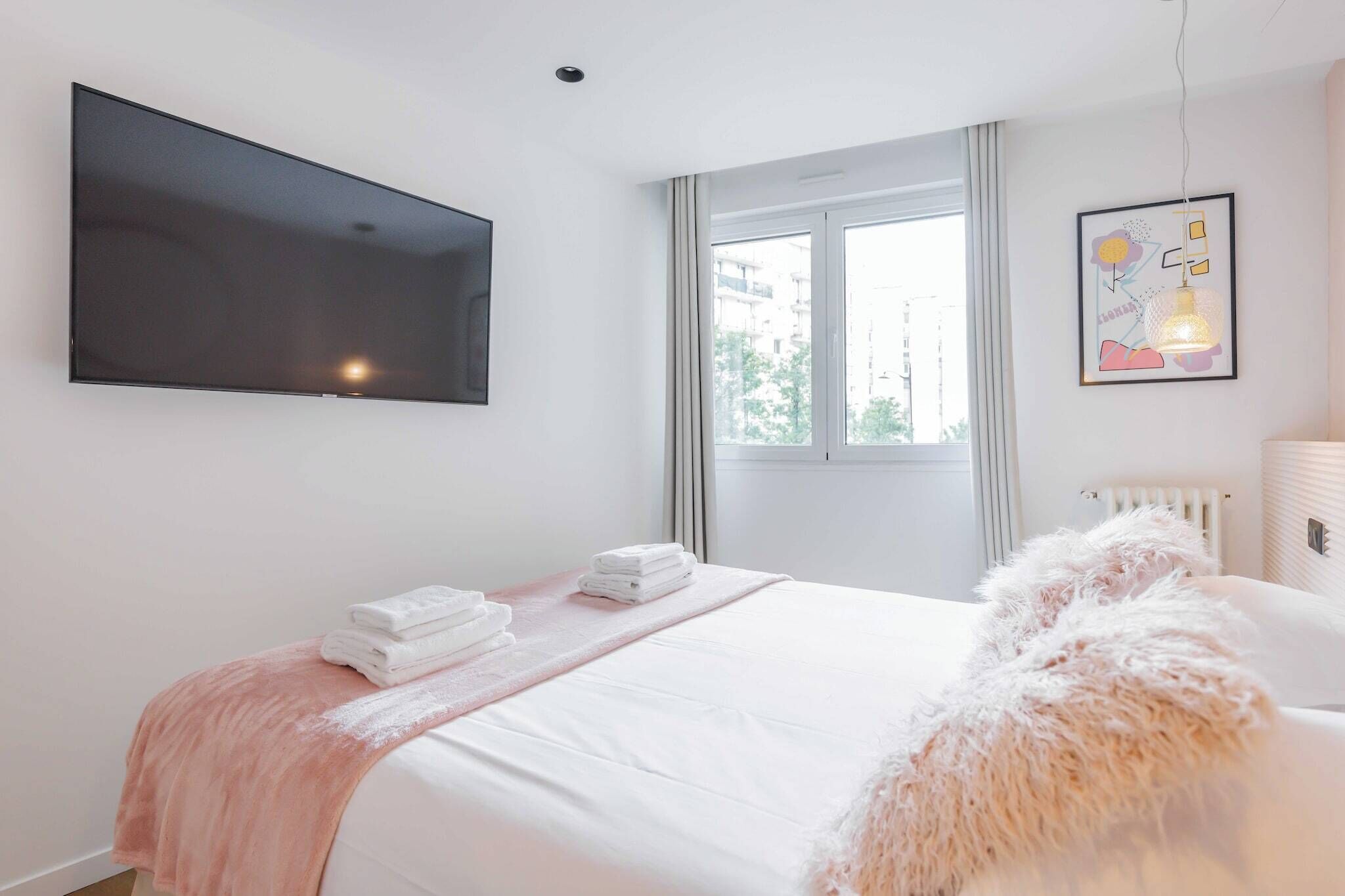 Ein Schlafzimmer mit einem Bett, einem flachbildfernseher an der Wand, einem Fenster mit Vorhängen und einer Heizung.
