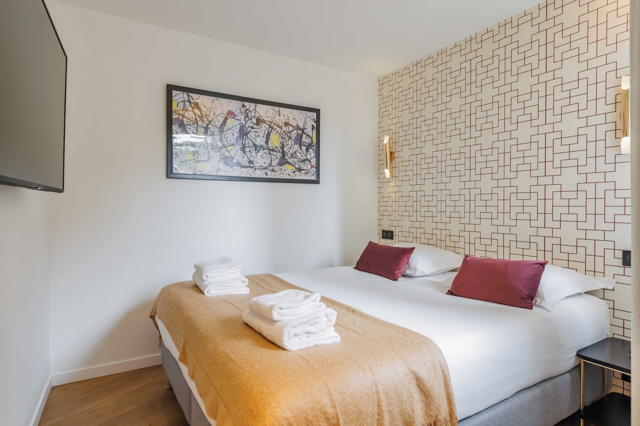 A hotel room with a bed, a painting on the wall, and a patterned wall.