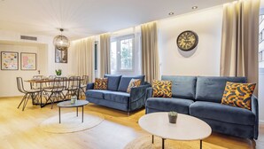 Un salon moderne avec un canapé bleu, une table à manger avec des chaises, une table basse et une grande fenêtre avec des rideaux.