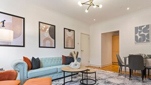Una sala de estar moderna con un sofá azul claro, un sillón naranja y un comedor con una mesa y sillas de vidrio.