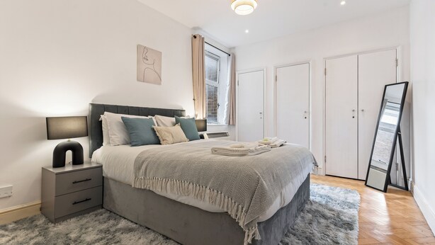 Un dormitorio con cama, mesitas de noche, un espejo y una ventana con cortinas.
