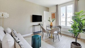 A modern living room with a sofa, chairs, a TV, a small table, and a potted plant. - Cosy apartment - 1BDR-4P - Ivry-sur-Seine (Ivry-sur-Seine)