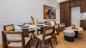 Un comedor moderno con una mesa redonda dispuesta para cuatro personas, rodeada de sillas de madera con asientos de mimbre. Un cuadro abstracto de gran tamaño adorna la pared sobre la mesa.