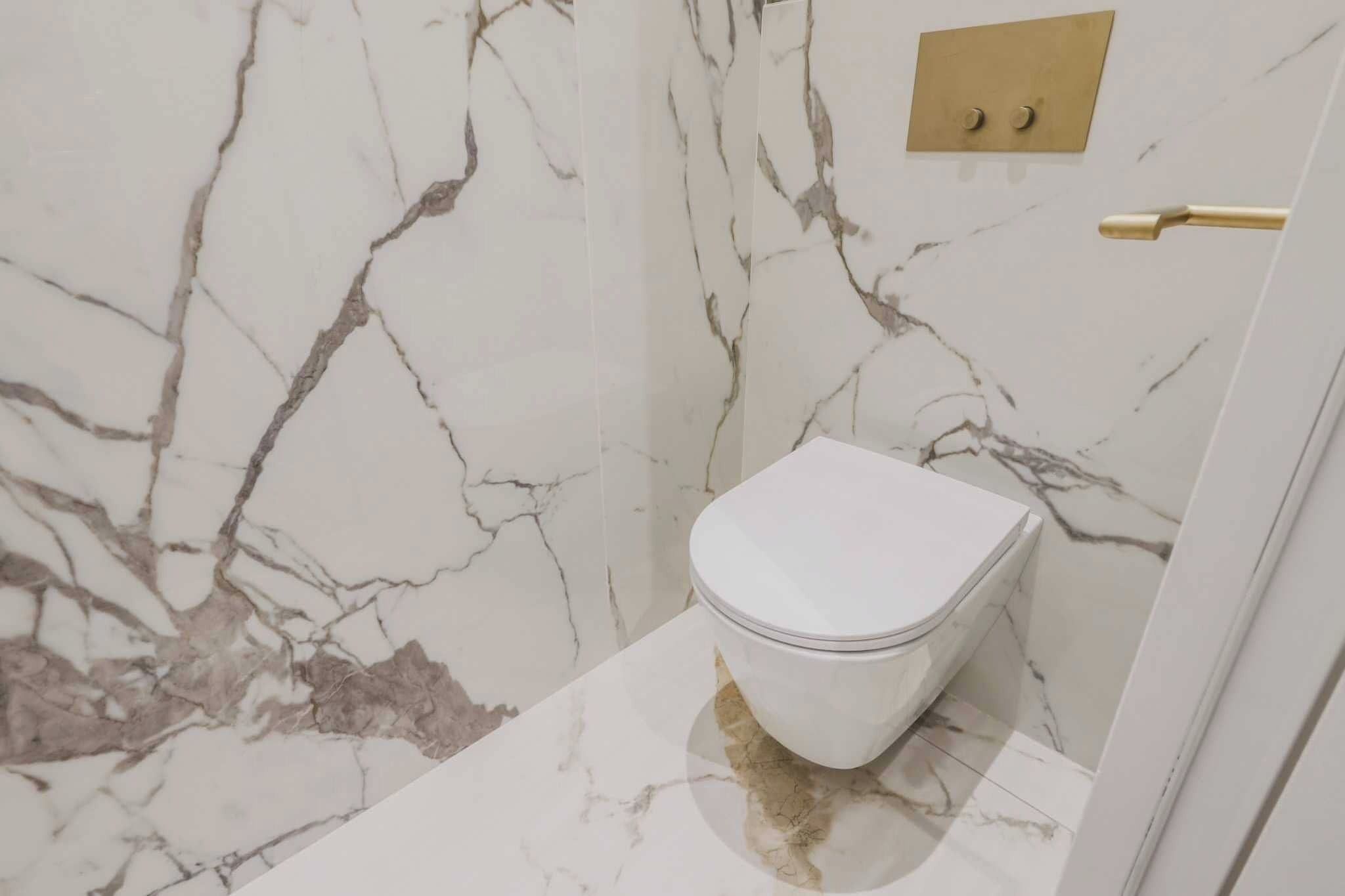 A bathroom with a marble wall and a toilet.