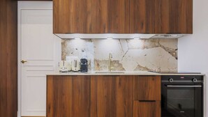 Una cocina con armarios de madera, encimera blanca, salpicadero de mármol, cafetera, fregadero y horno empotrado.