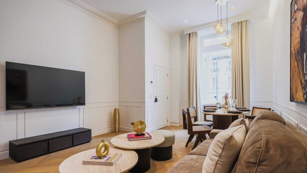 Una sala moderna con un televisor de pantalla plana, un sofá, una mesa de centro y un comedor con sillas y una mesa.