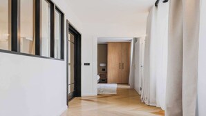 A hallway with wooden flooring and white walls, leading to a room with a bed and a wardrobe.