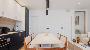 A modern kitchen with black cabinets, a white countertop, and a dining area with a long table and chairs.