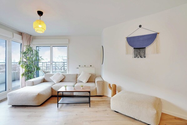Un salon moderne avec un canapé d’angle, une petite table basse et une décoration murale en macramé.