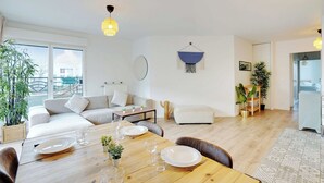 Ein modernes Wohnzimmer mit einer Couch, einem Esstisch für zwei Personen und einer Hängeleuchte.