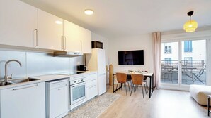 Eine moderne Küche mit weißen Schränken, einem Backofen und einem Geschirrspüler. Es gibt einen Essbereich mit Tisch und Stühlen sowie ein großes Fenster mit Blick auf die Stadt.