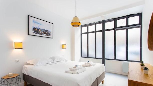 A modern hotel room with a large bed, bedside lamps, a cityscape picture, and a large window with frosted glass. - Magnificent apartment - 1BR/4P - Picpus (Paris)