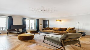 Ein modernes Wohnzimmer mit einer Couch, einem Sessel, einem Hocker und einem Flachbildfernseher.