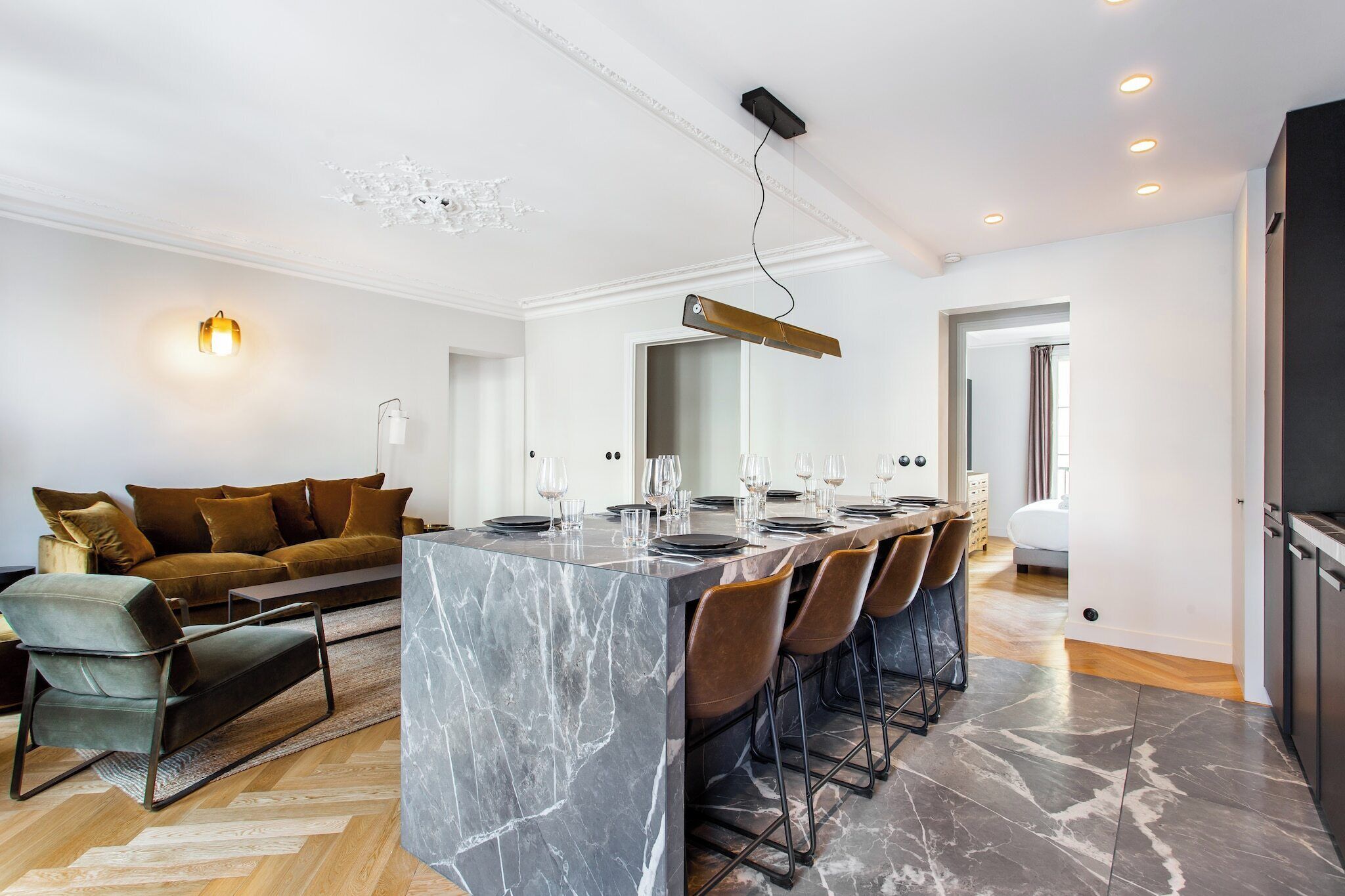 A modern kitchen with a marble island, bar stools, and a dining area.