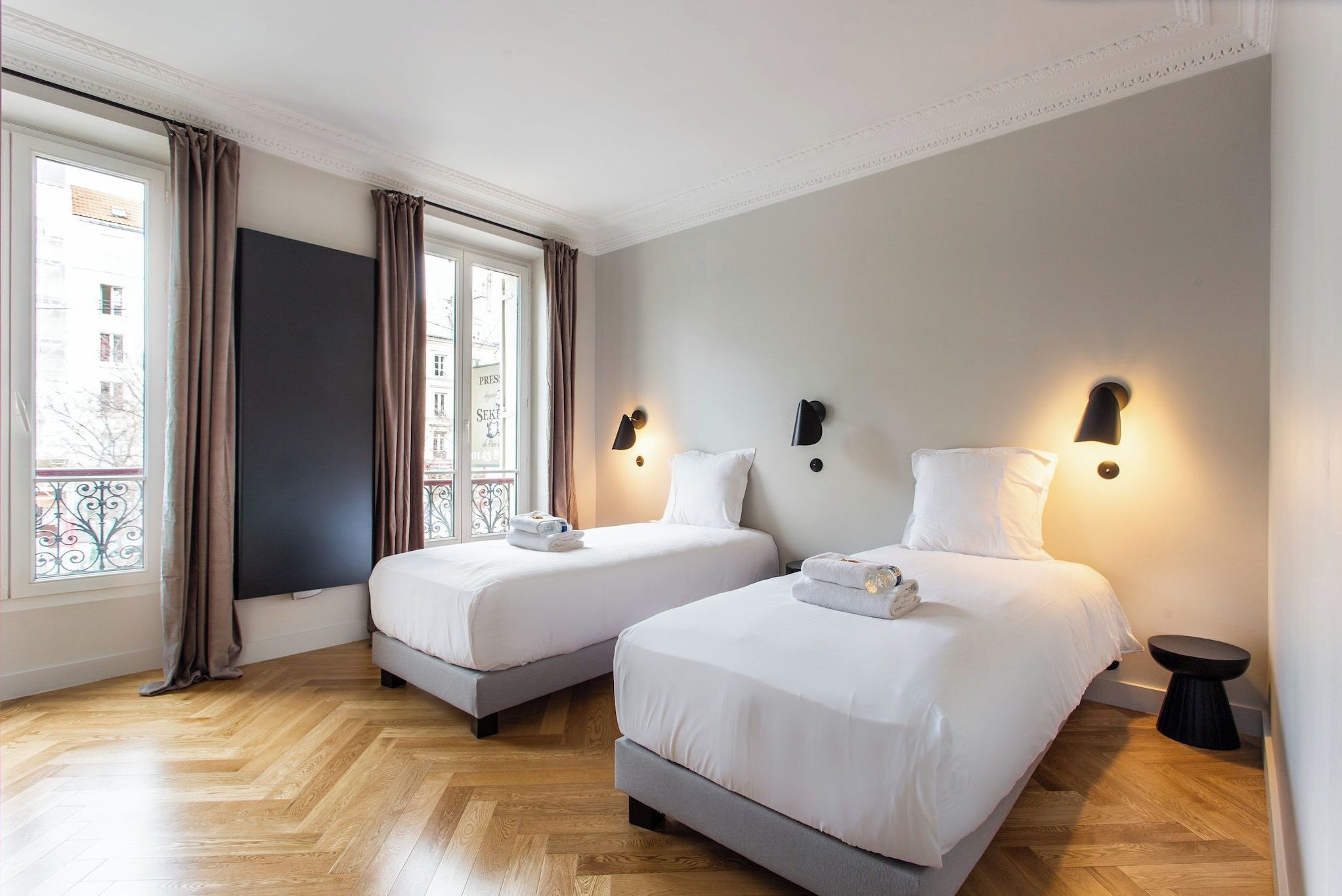 A hotel room with two beds, a large window with curtains, and a view of buildings outside.