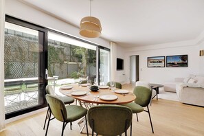 A modern dining area with a round table set for four, surrounded by green chairs, large windows, and a view of the outdoor patio.